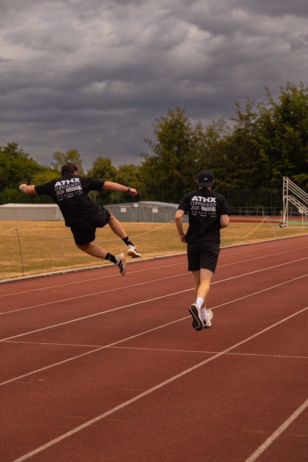 One member leaping while another jogs beside him on the track