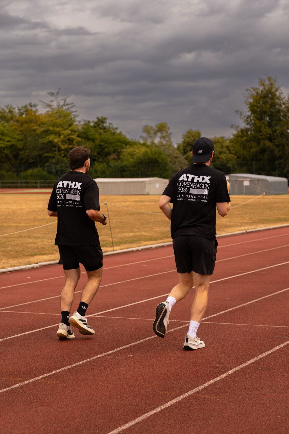 Two members running side by side on a track under a grey sky